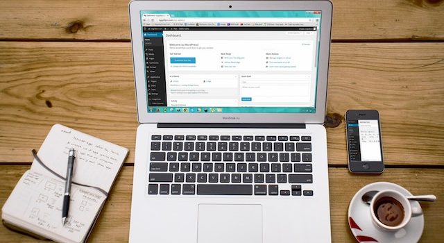 Laptop dengan dasbor admin WordPress dibuka di atasnya yang terletak di atas meja kayu