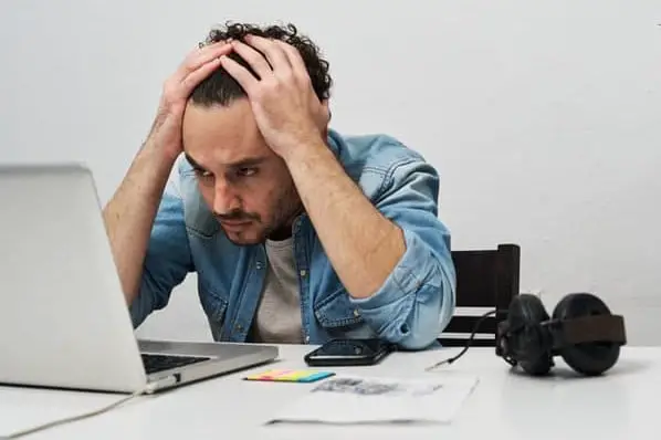 L'homme regarde un ordinateur portable avec ses mains sur sa tête alors qu'il fait face à l'épuisement professionnel