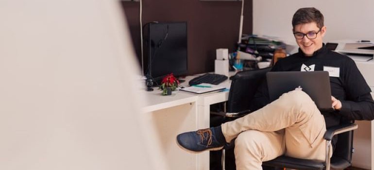 Uomo seduto su una sedia, guardando il suo laptop e sorridente